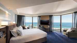 A hotel room with a large bed, a desk, a TV, and a view of the ocean.