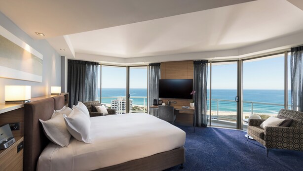 A hotel room with a large bed, a desk, a TV, and a view of the ocean. - Sofitel Gold Coast Broadbeach (Broadbeach)