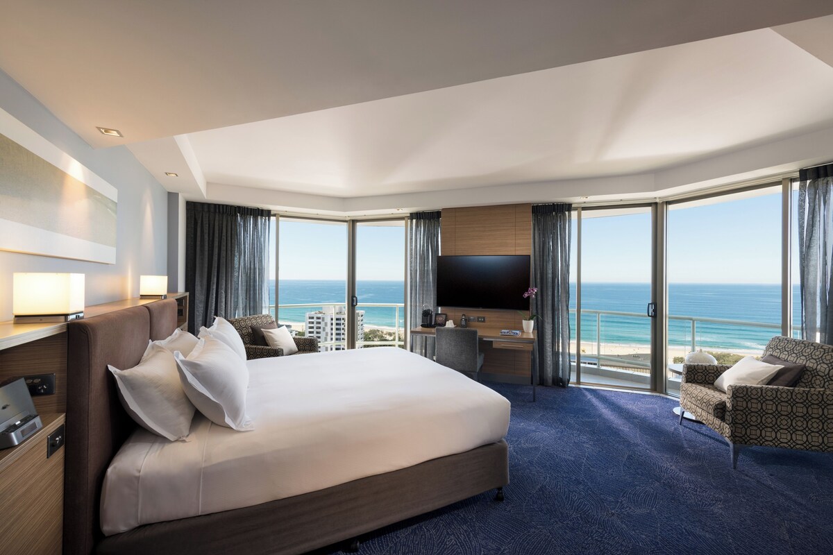 Une chambre d’hôtel avec un grand lit, un bureau, une télévision et une vue sur l’océan.