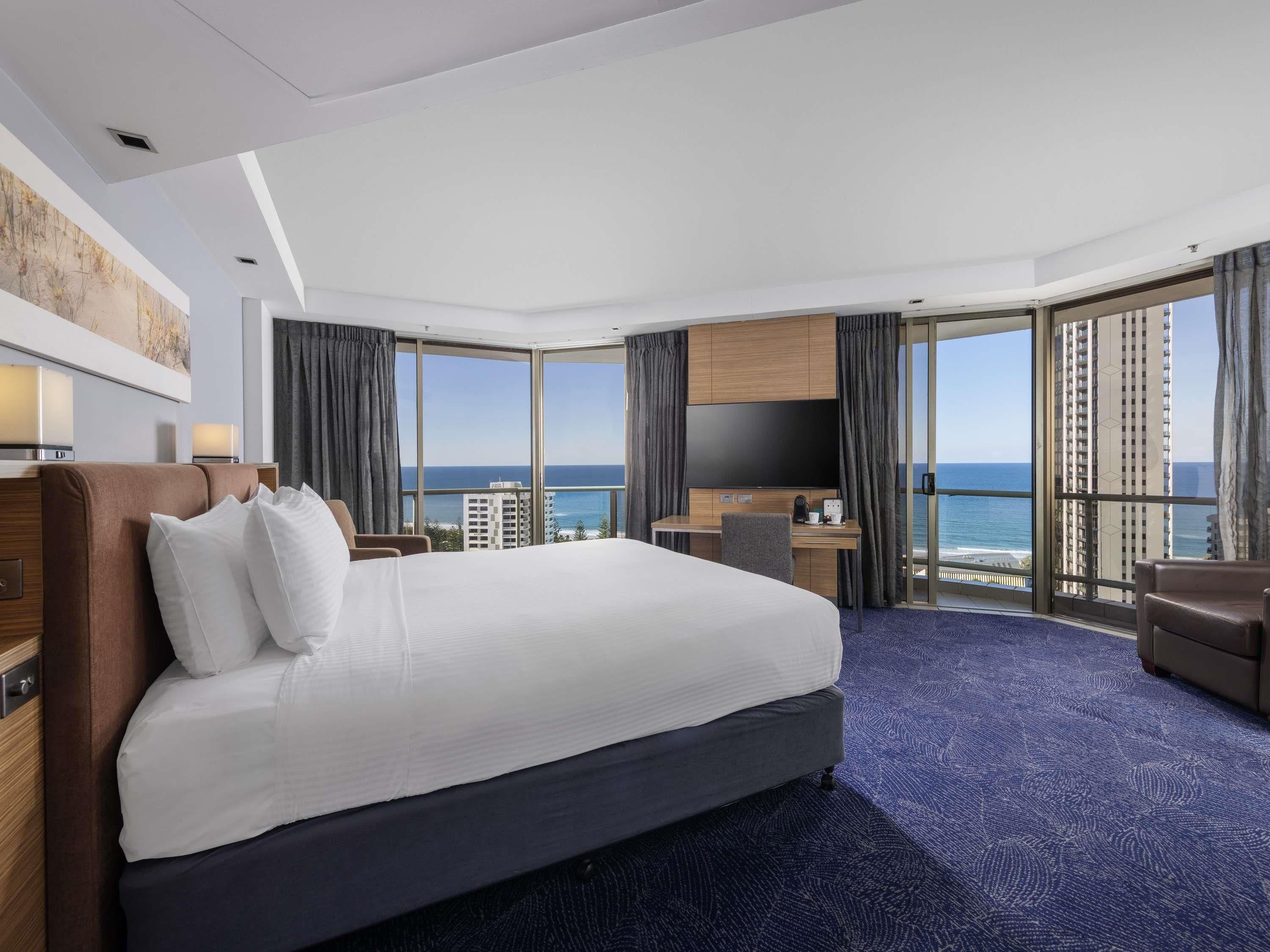 Een hotelkamer met een groot bed, een bureau, een televisie en uitzicht op zee.