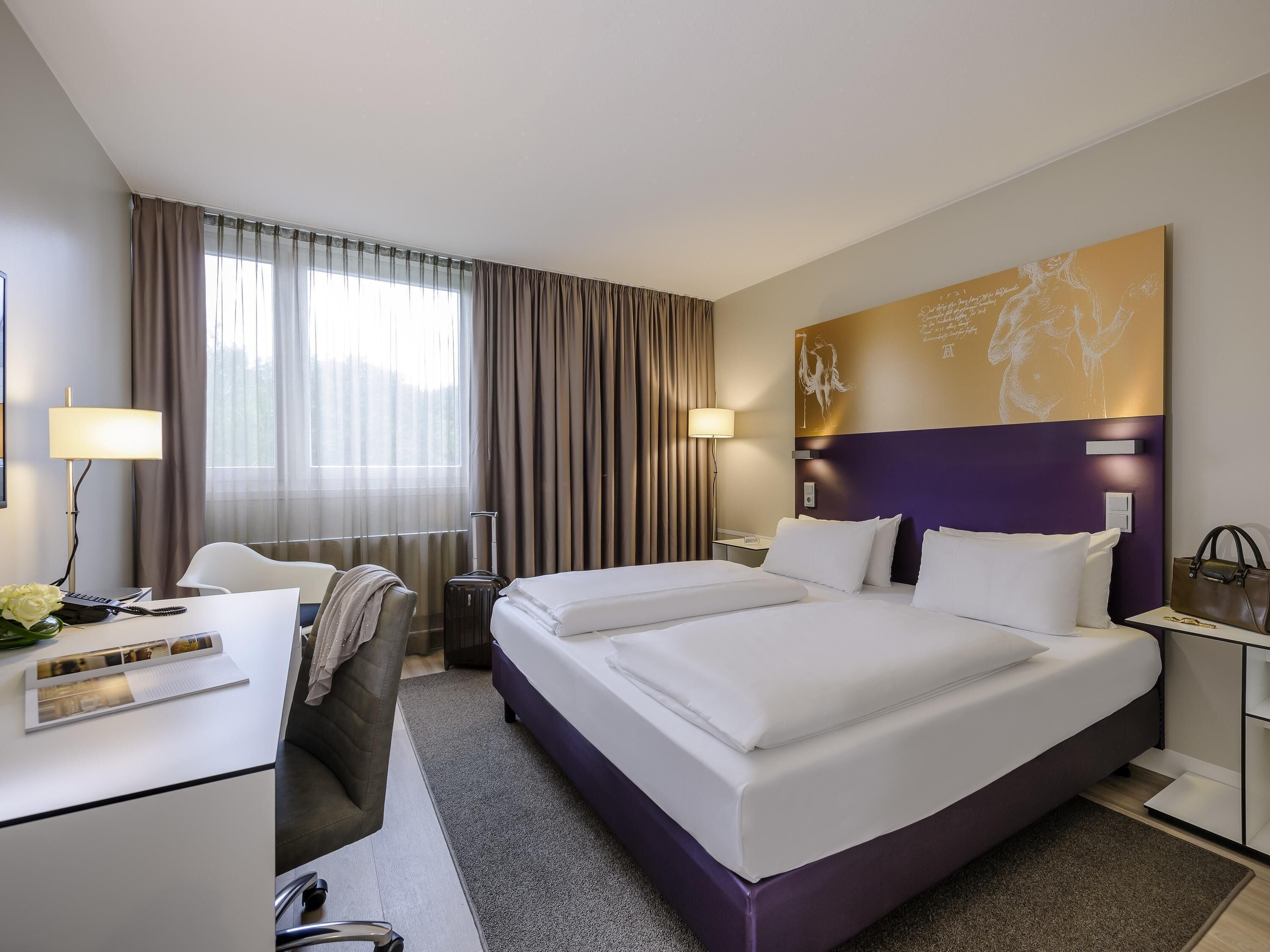 A hotel room with a large bed, a desk with a chair, a lamp, and a window with curtains.