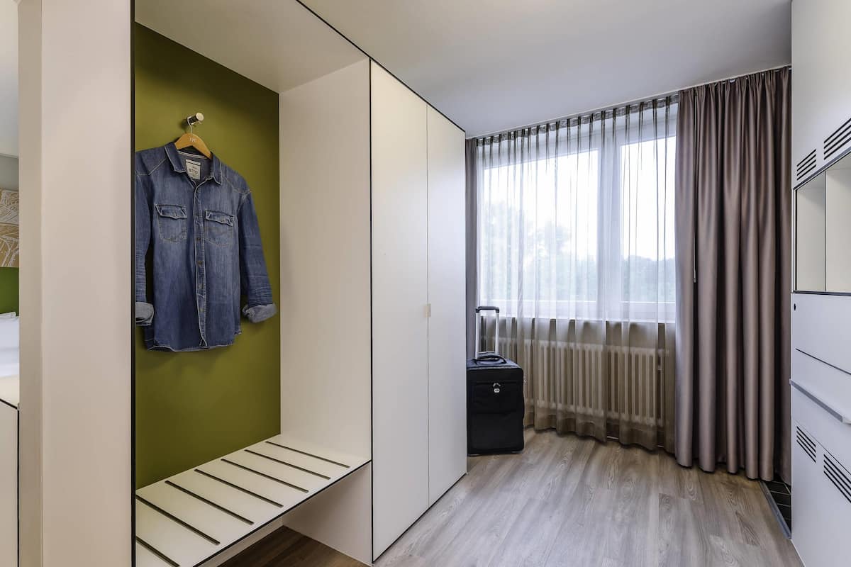 Una habitación de hotel moderna con vestidor, un banco, una maleta y una ventana con cortinas.
