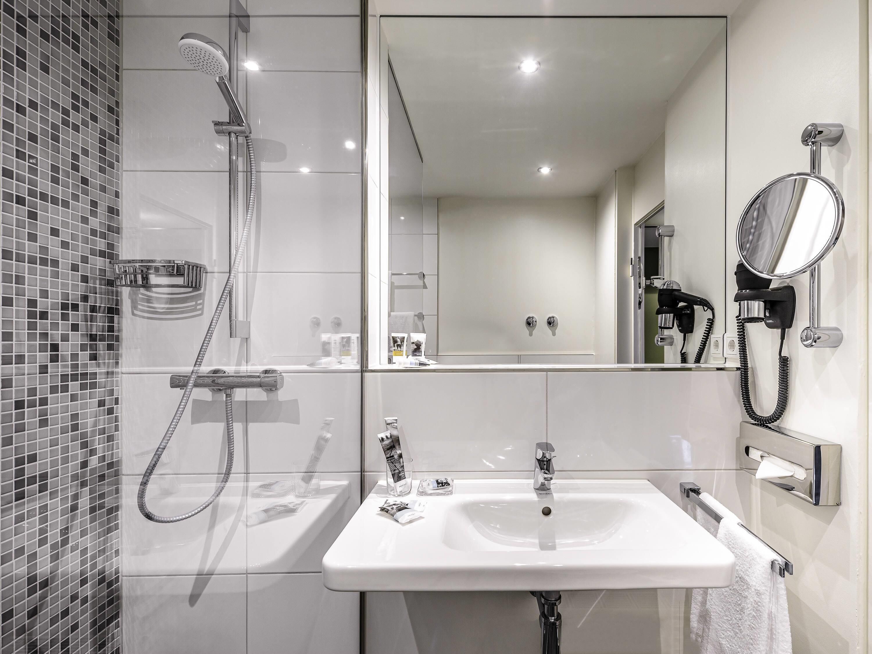 Un baño moderno con ducha, lavamanos, espejo y toallero.