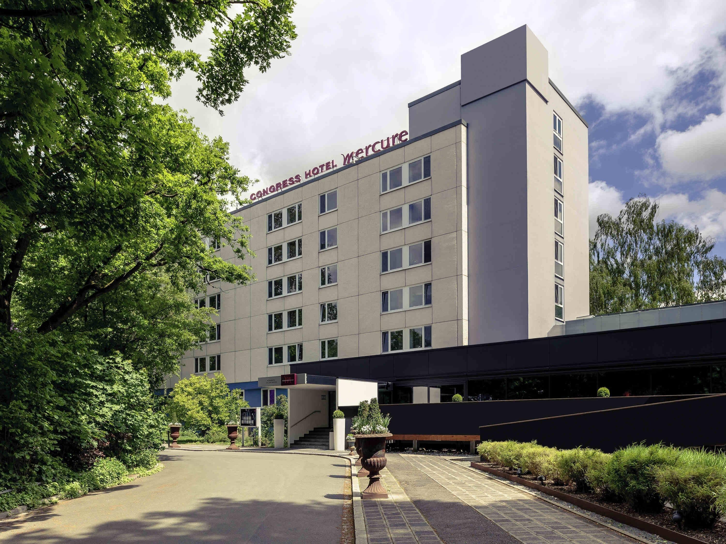 A multi-story hotel with a modern design, featuring a prominent entrance with a staircase and a large planter.