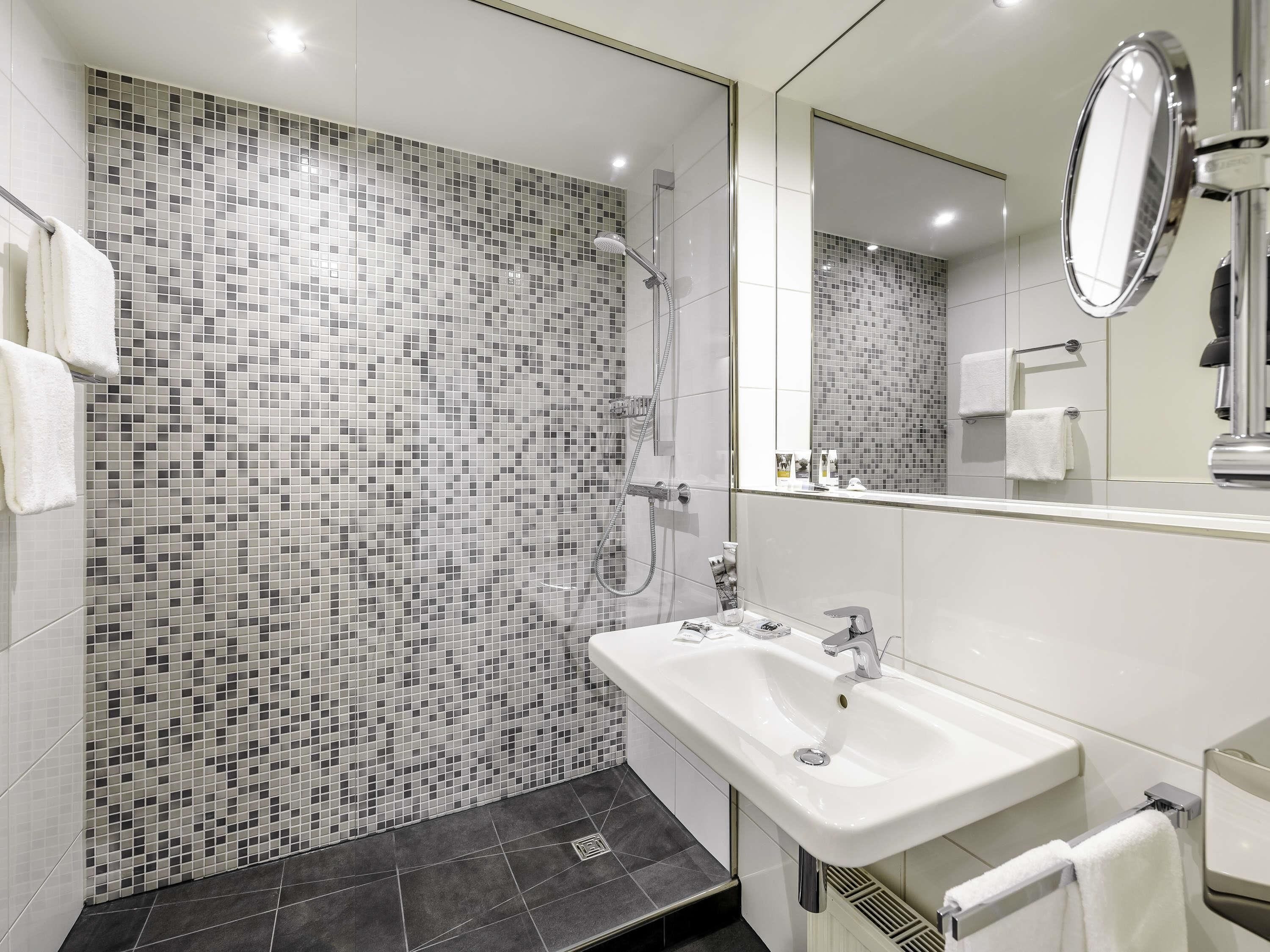 Un baño moderno con pared de mosaicos, ducha, lavamanos y espejo.