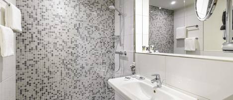 Un baño moderno con pared de mosaicos, ducha, lavamanos y espejo.