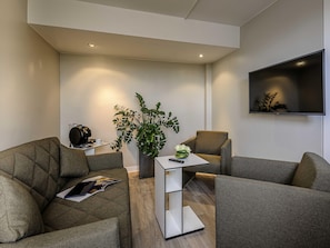 A modern living room with a sofa set, a coffee table, a plant, and a flat-screen TV mounted on the wall.