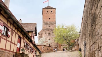 Una calle adoquinada que conduce a una torre histórica con una bandera, flanqueada por edificios tradicionales con entramado de madera.