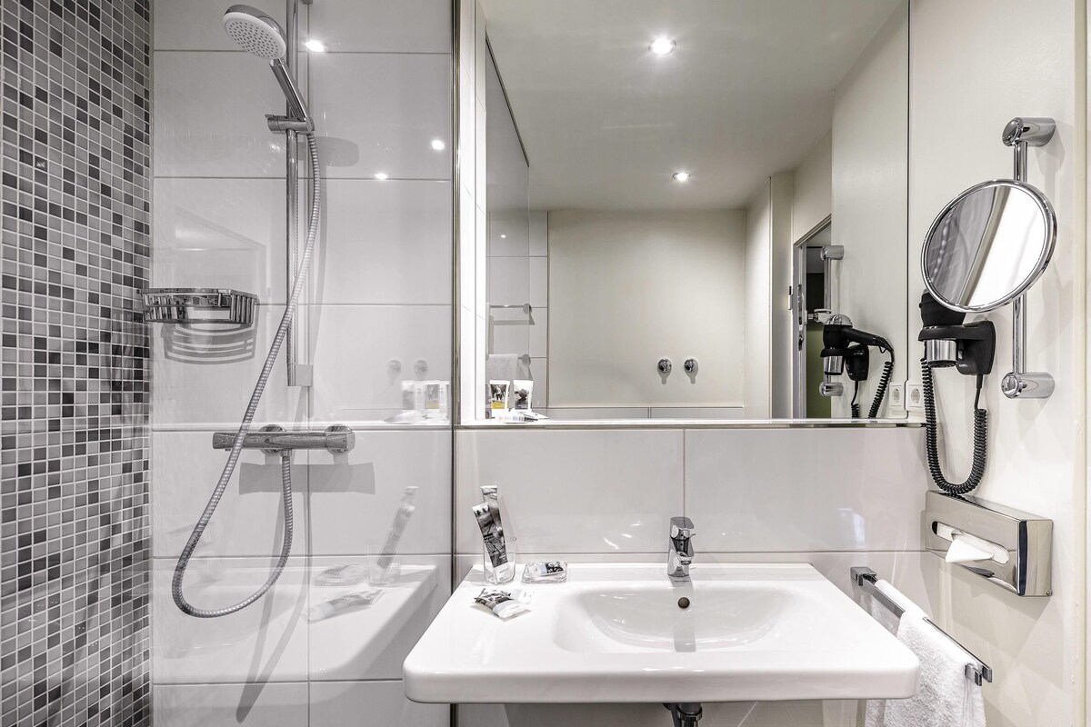 A modern bathroom with a shower, sink, mirror, and towel rack.