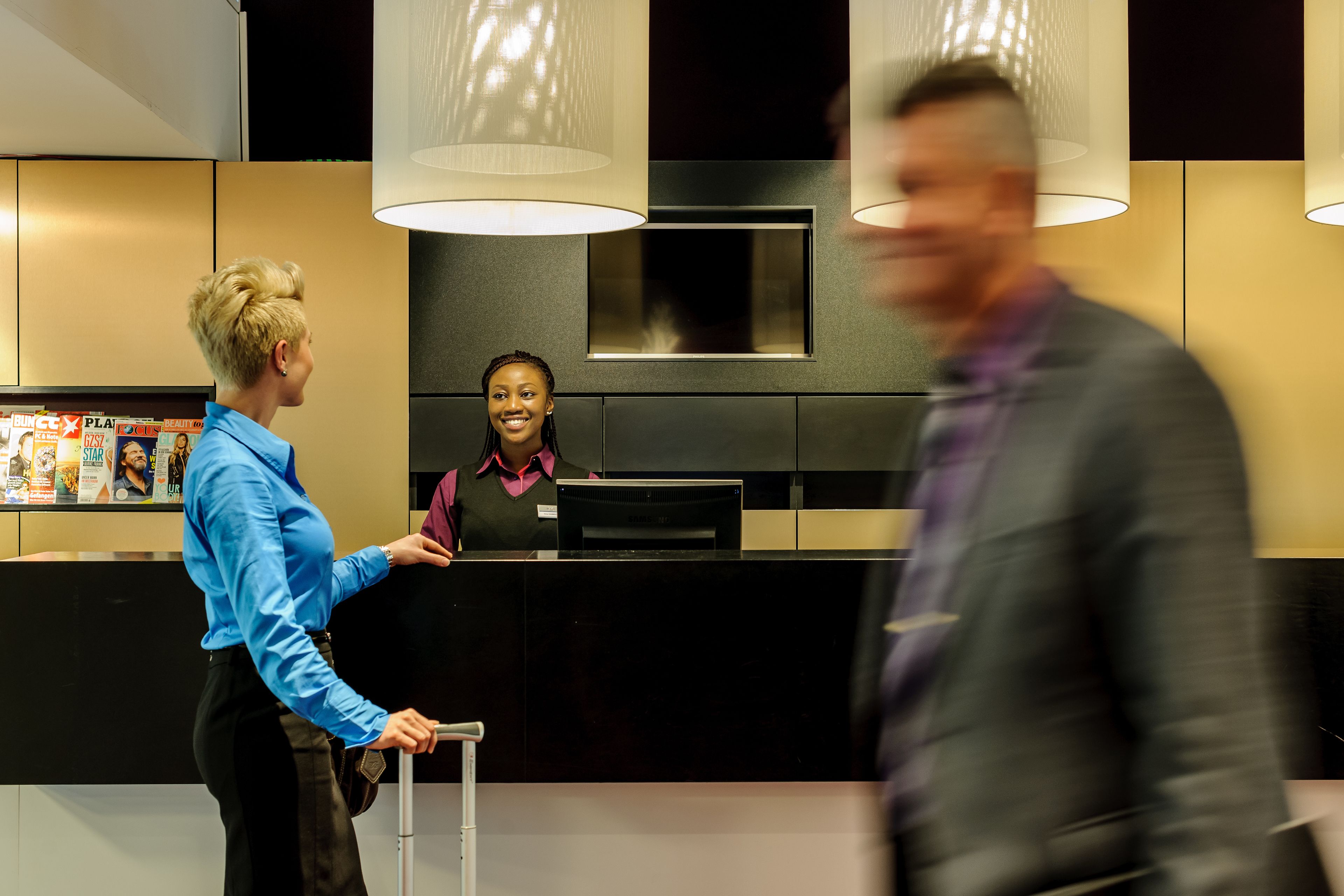 A hotel reception area with a black counter, a woman in a blue shirt, and a man in a suit.