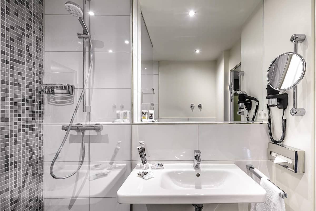 Un baño moderno con ducha, lavamanos, espejo y toallero.