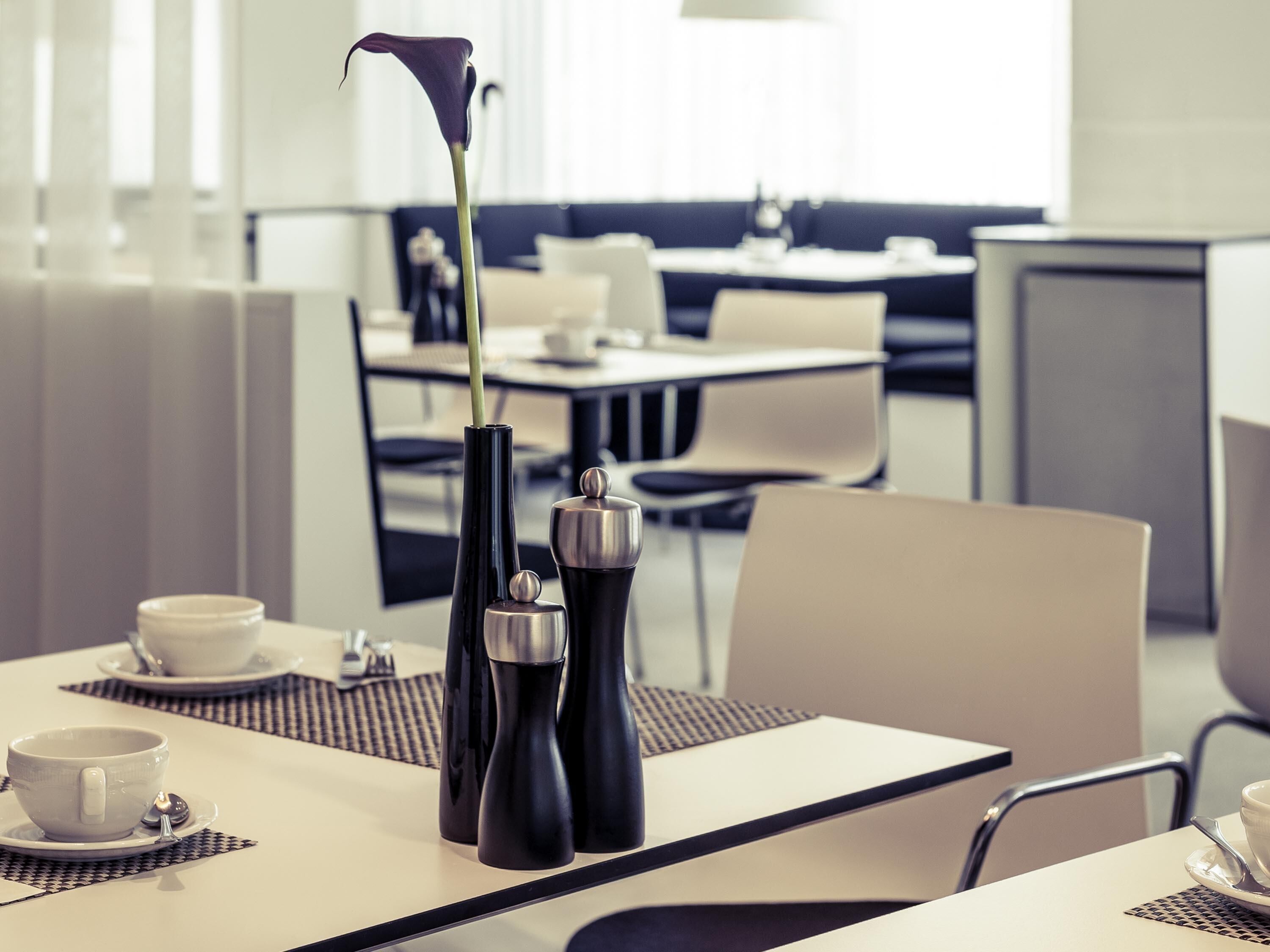 A modern dining area with tables, chairs, and a vase with a single flower.
