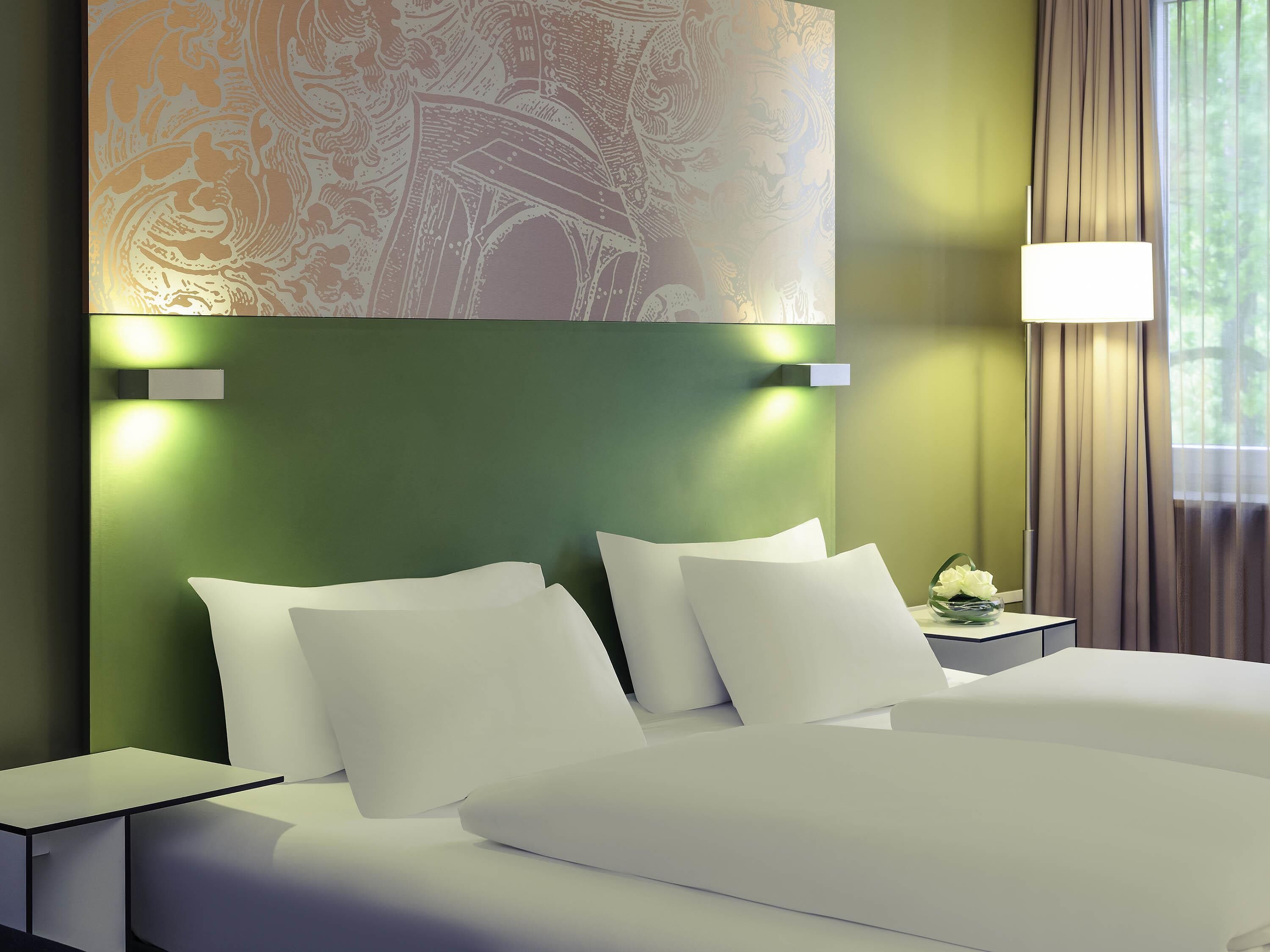 Una habitación de hotel con cama, almohadas, una mesita de noche, una lámpara y una pared con diseño decorativo.