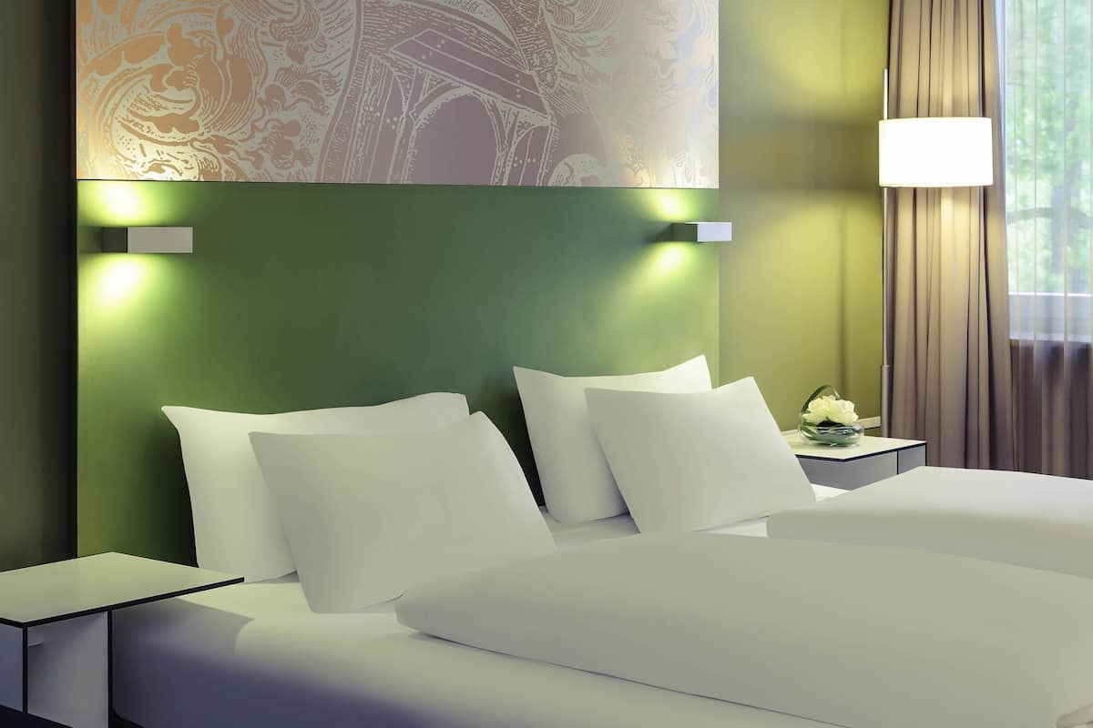 Una habitación de hotel con cama, almohadas, una mesita de noche, una lámpara y una pared con diseño decorativo.