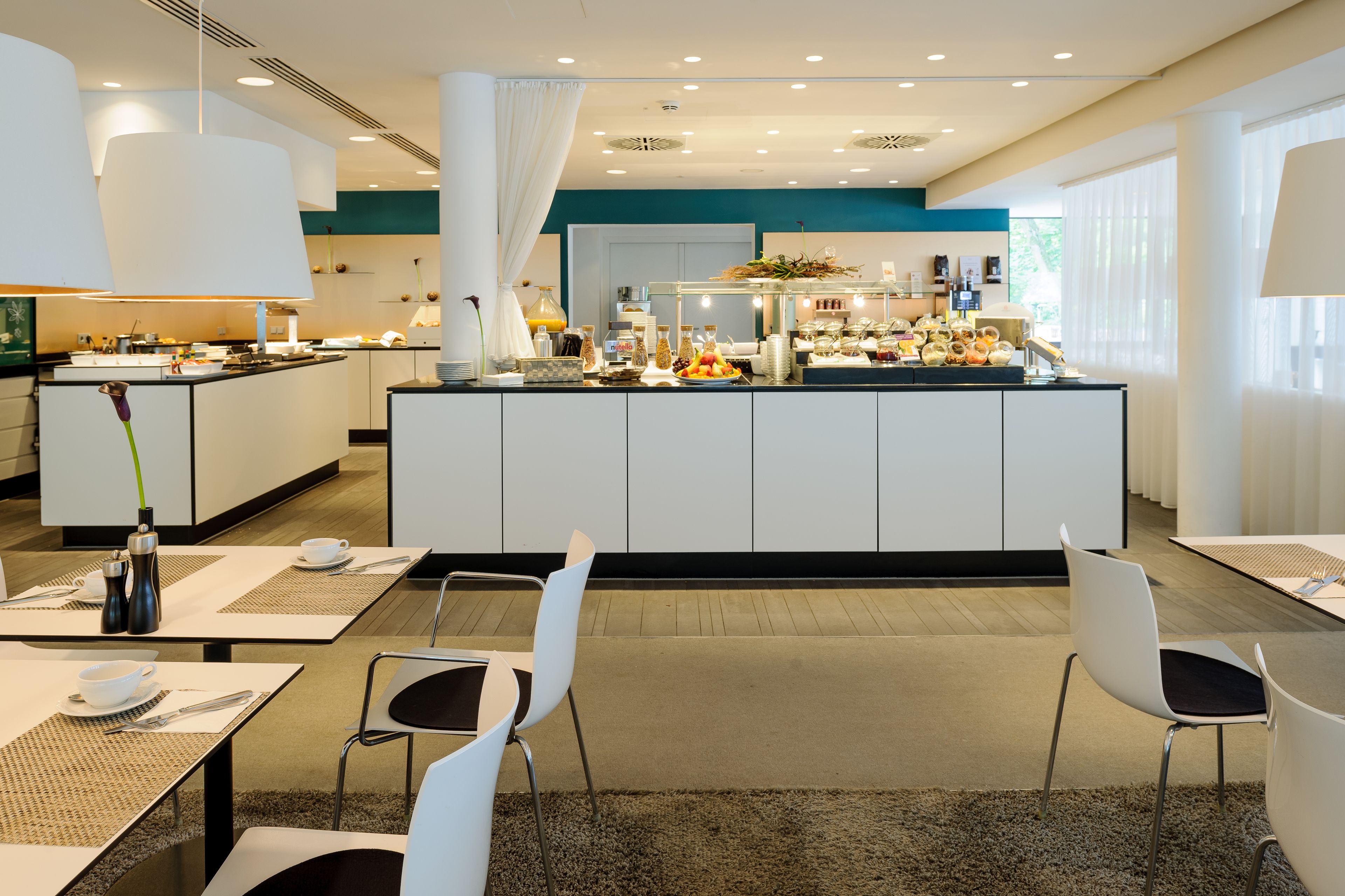 Een moderne hotel eetruimte met een buffet, witte meubels en een zicht op de keuken op de achtergrond.