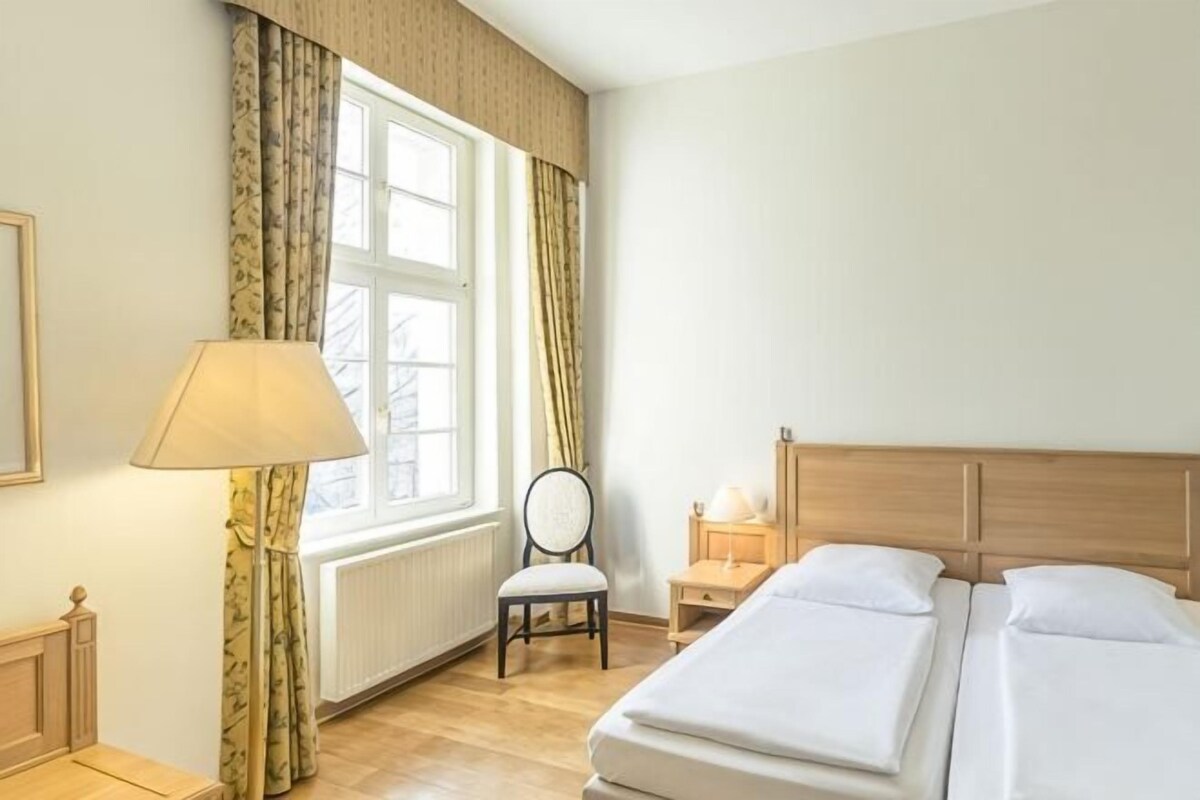 A hotel room with a bed, a chair, a lamp, a nightstand, and a window with curtains.