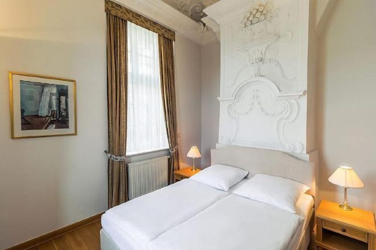 A double bed with two bedside tables, a window with curtains, and a framed picture on the wall.