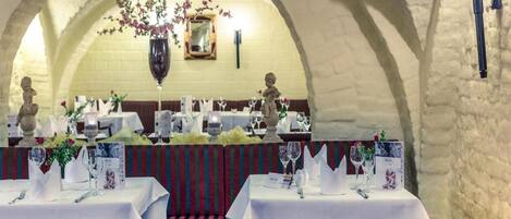 An indoor dining area with tables set for service, a chandelier, and stone arches.