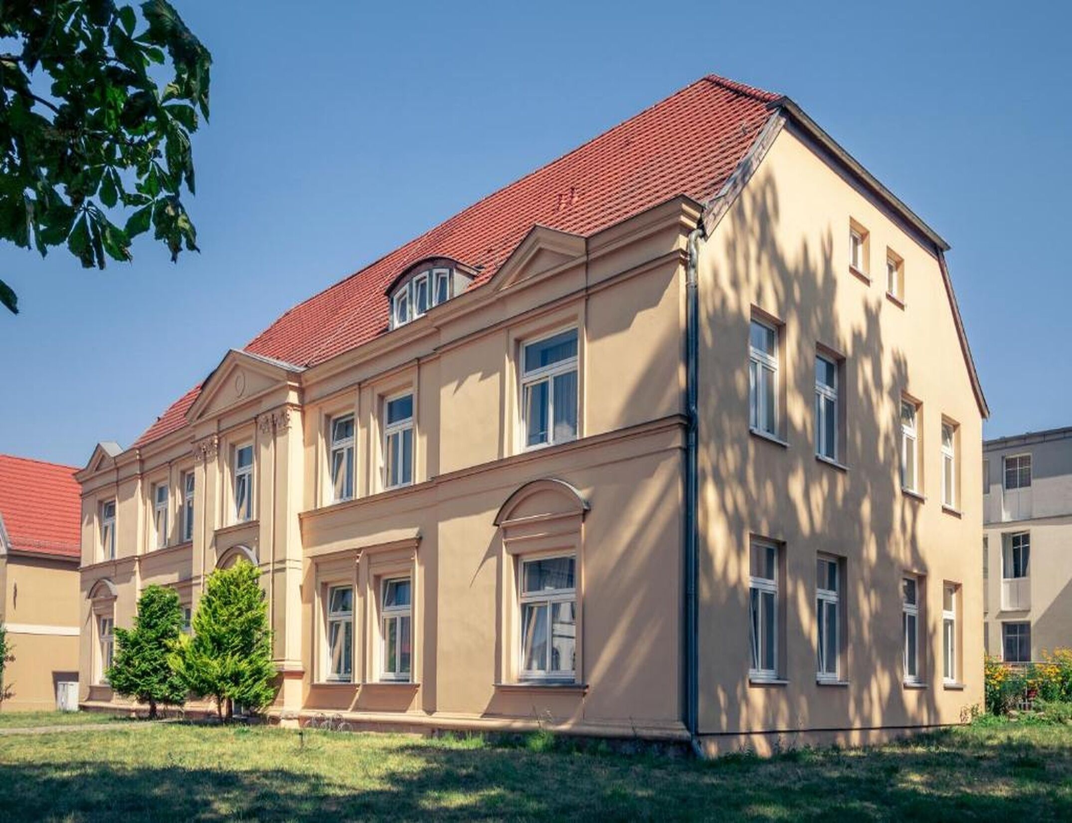 A multi-story building with a red-tiled roof, large windows, and a symmetrical facade.