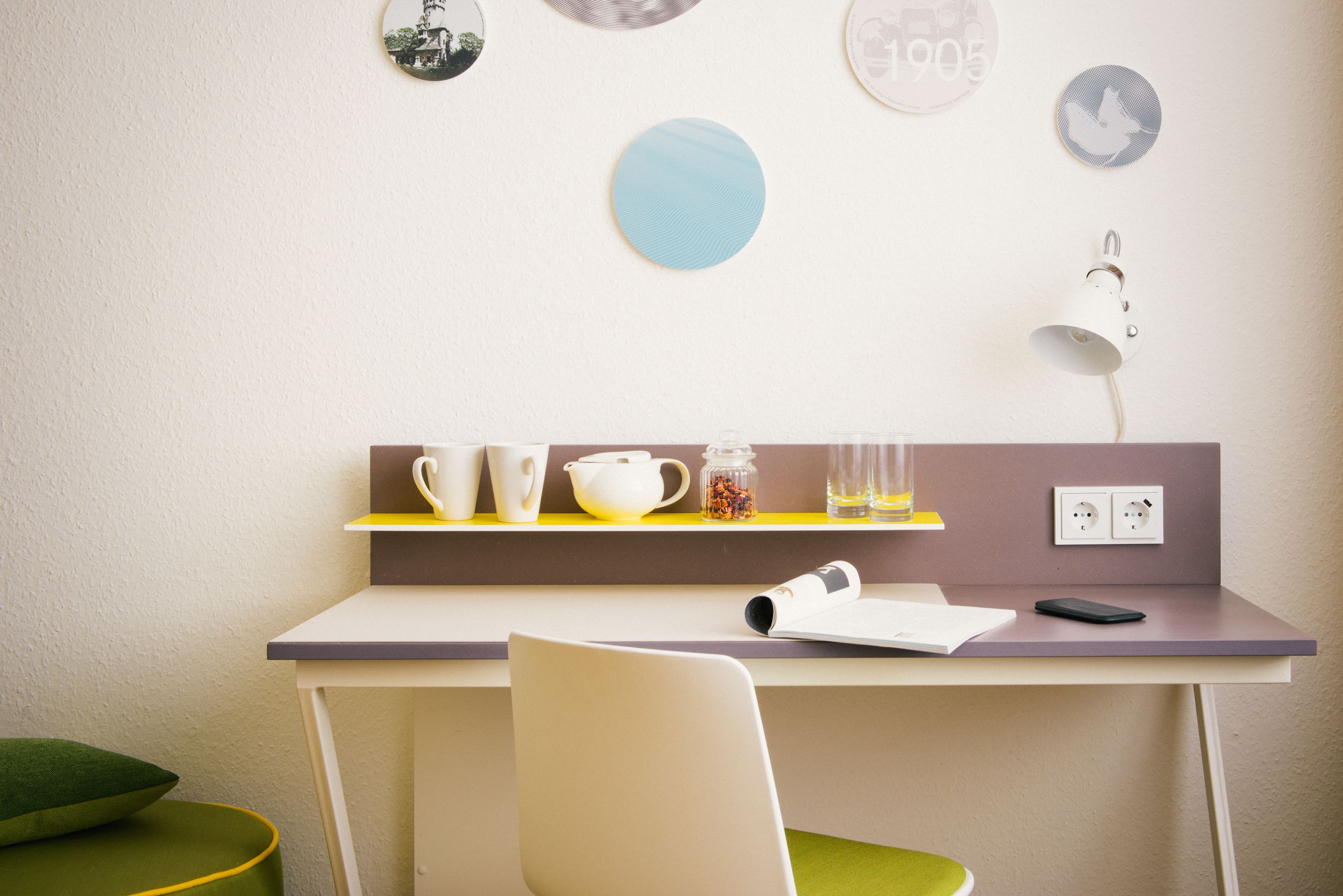 Quarto moderno com escrivaninha, cadeira e prateleira com xícaras e abajur.