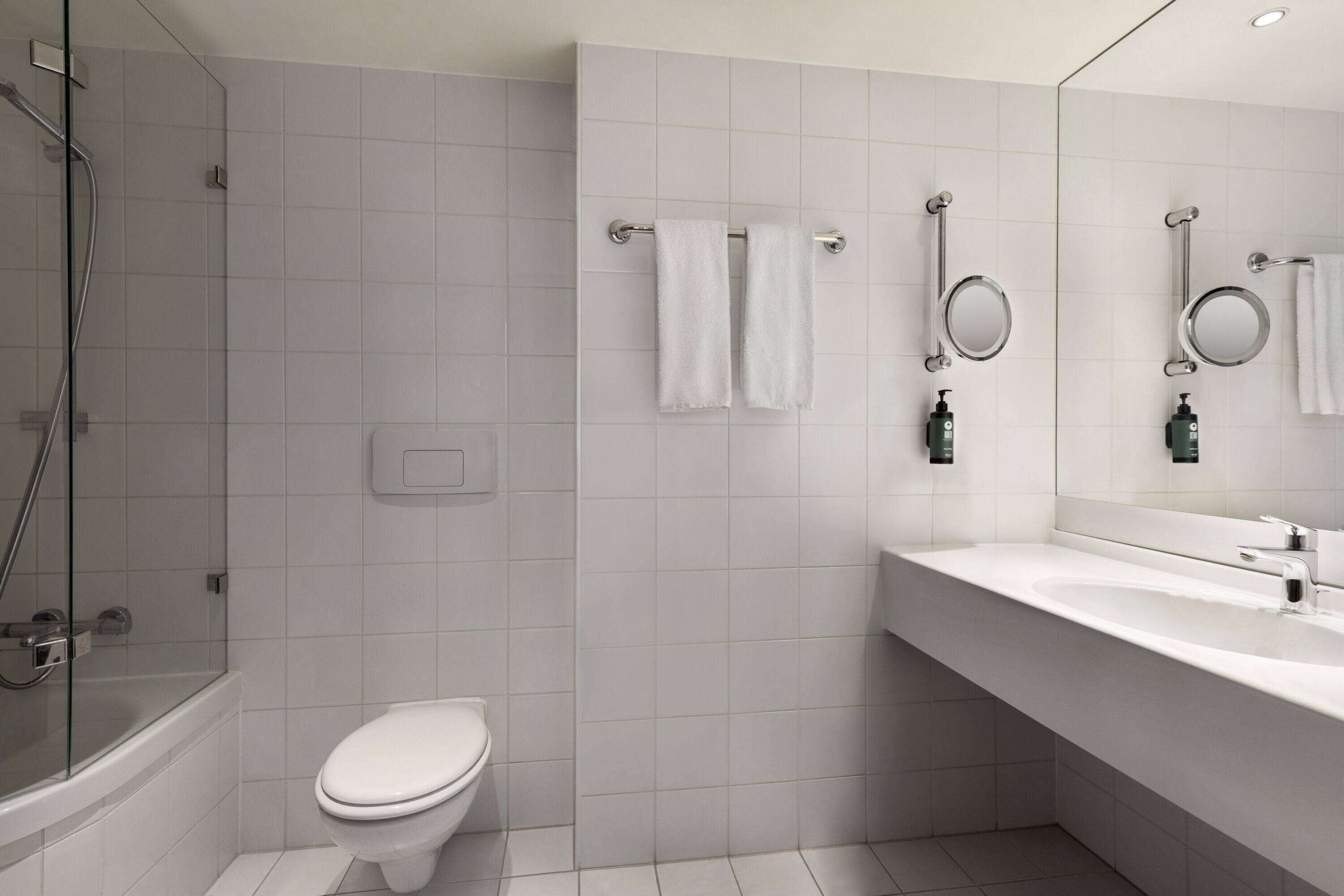 Un baño moderno con ducha envuelta en vidrio, un inodoro blanco, un lavabo con espejo y dos toallas colgadas en un perchero.