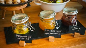 Three jars of preserves labeled mango-lime-chili, apple-birne-anas, and erdberee strawberry on a wooden table.