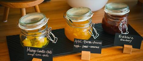 Tres botes de conservas etiquetados con mango-lima-chile, manzana-birne-anas y erdberee fresa sobre una mesa de madera.