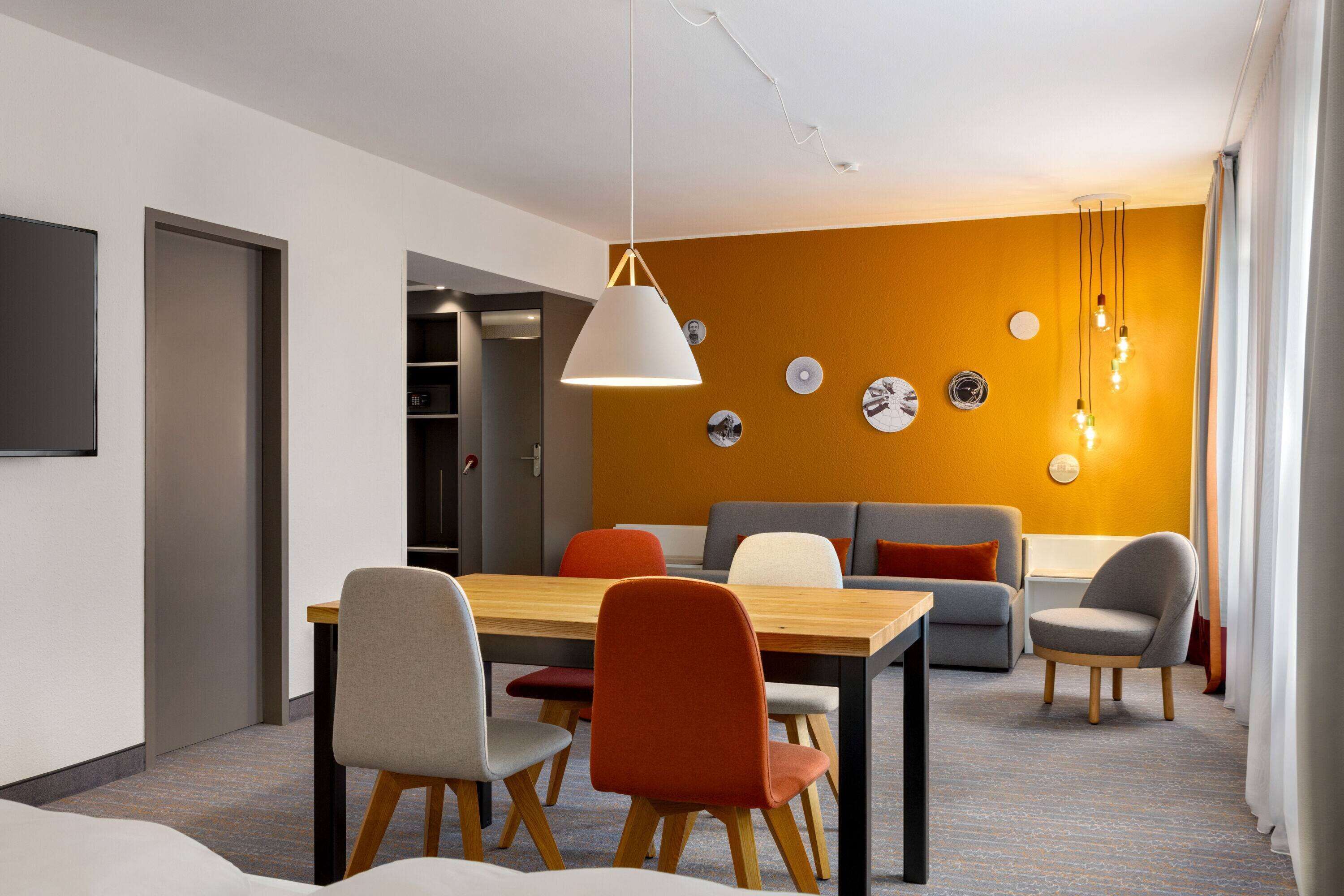 Habitació d'hotel moderna amb zona de menjador, seients de sofà i una paret decorada amb plats.