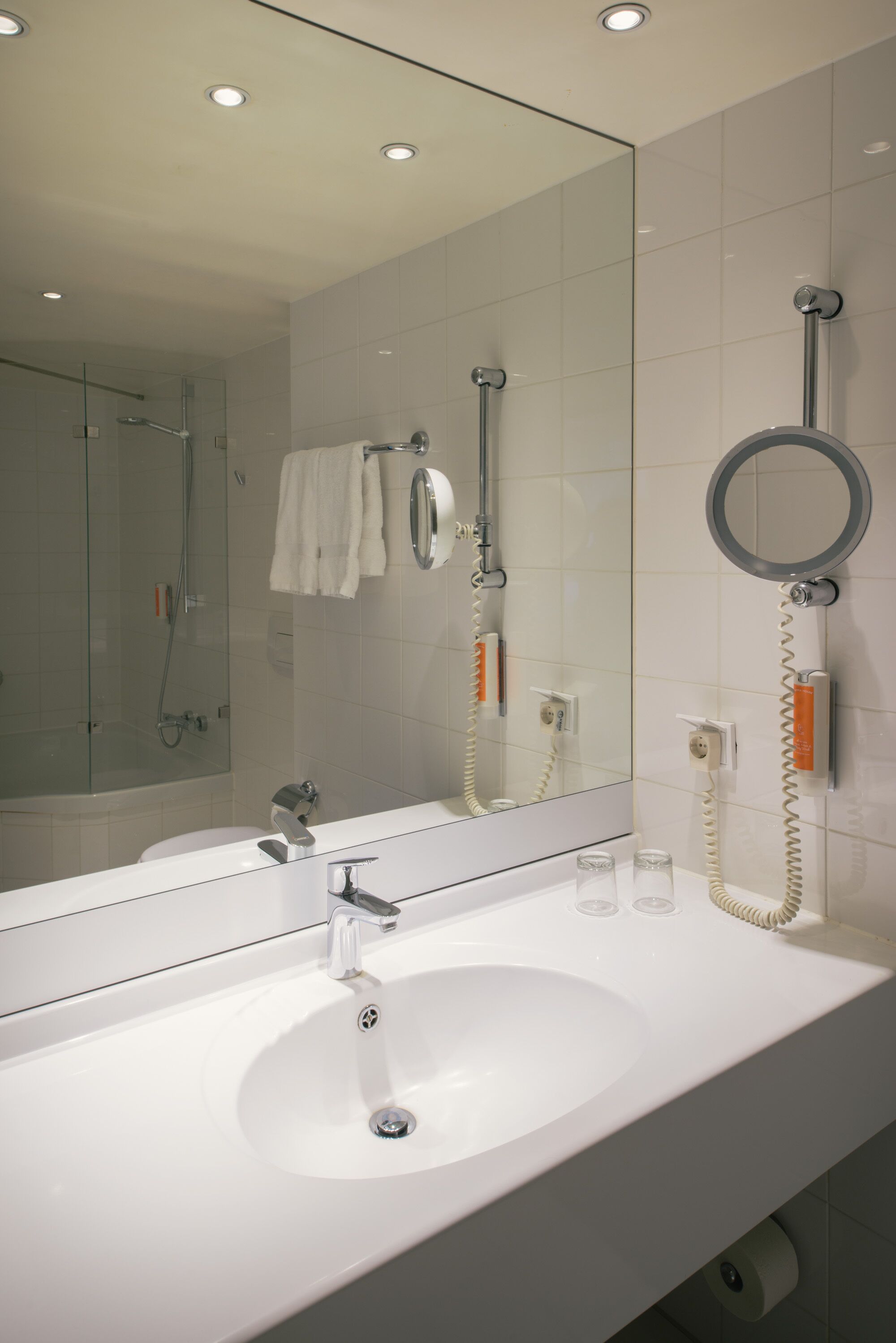 A modern bathroom with a white sink, a large mirror, and a handheld showerhead.