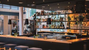 A bar area with stools, shelves of bottles, and hanging plants. - Vienna House Easy by Wyndham Bad Oeynhausen (Bad Oeynhausen)