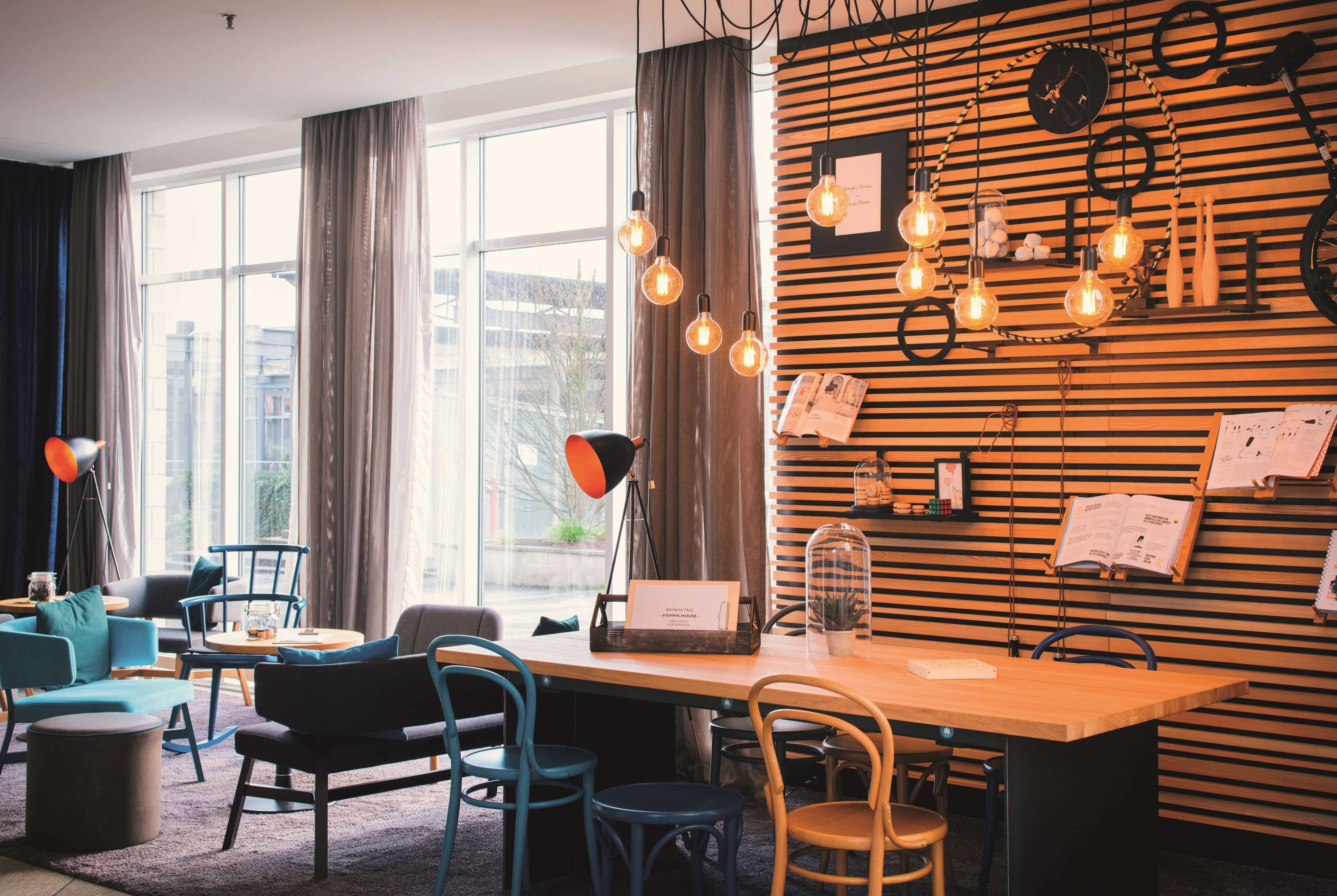 Un espacio de trabajo moderno con un panel de listones de madera, bombillas colgantes y un ordenador portátil sobre una mesa.