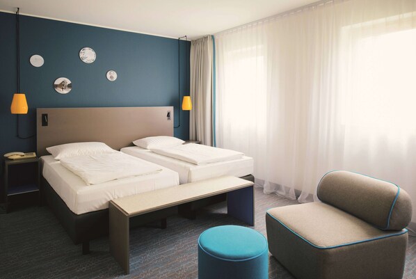 A hotel room with two beds, a desk, a chair, and a small ottoman.