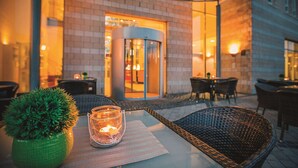 An outdoor seating area with wicker chairs and a table, a potted plant, and a lit candle. - Vienna House Easy by Wyndham Bad Oeynhausen (Bad Oeynhausen)