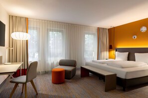 Ein modernes Hotelzimmer mit einem großen Bett, einem Schreibtisch, einem Sessel und einem kleinen Tisch.