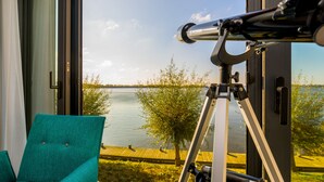 Une pièce avec un télescope, un fauteuil de couleur turquoise et une vue sur un lac.