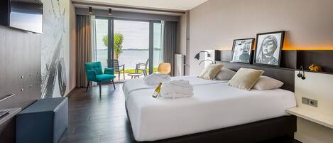 A modern hotel room with a large bed, a TV mounted on the wall, and a view of the water outside.