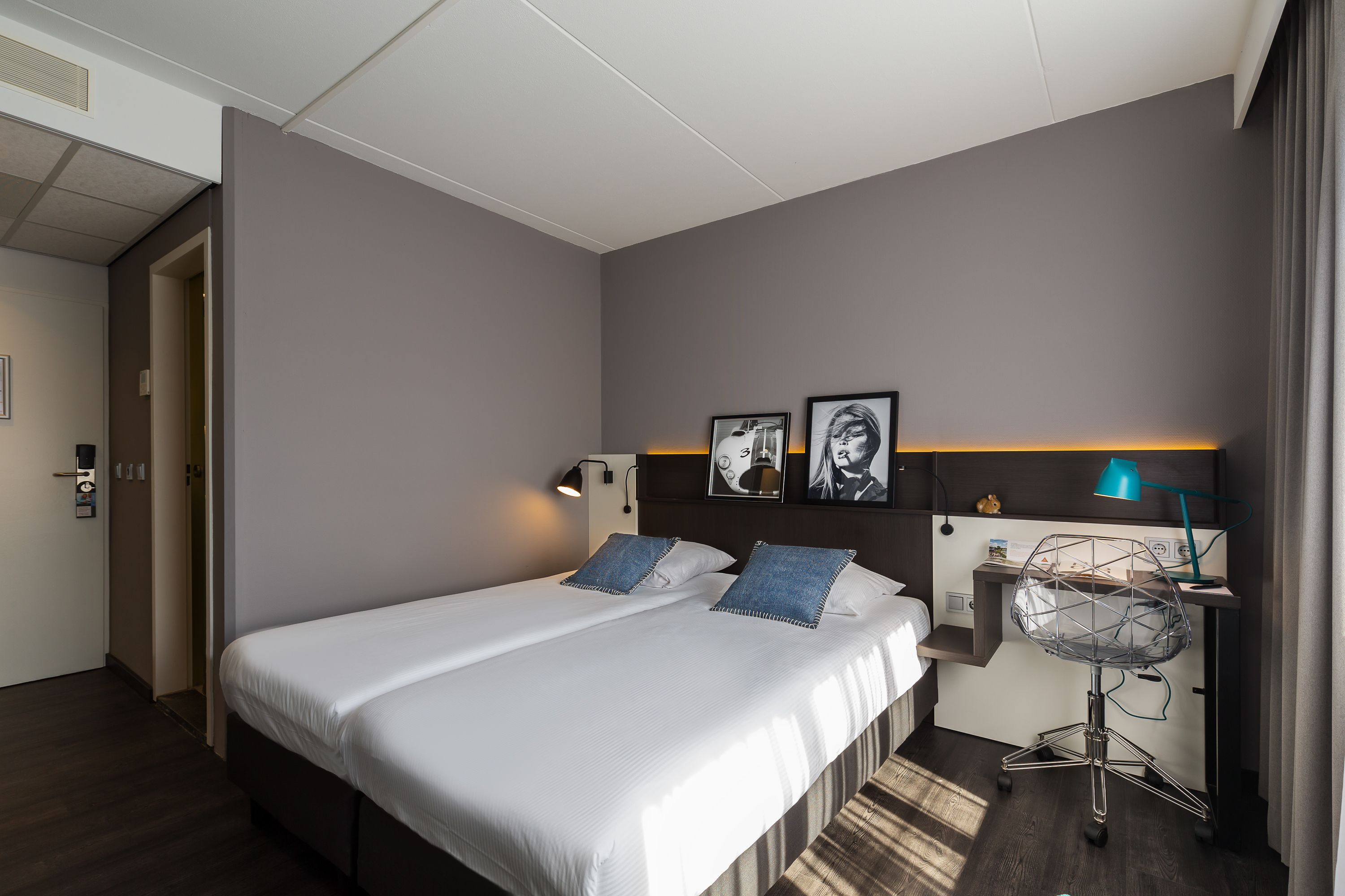 Una habitación de hotel con una cama grande, un escritorio con silla y una lámpara de pared.