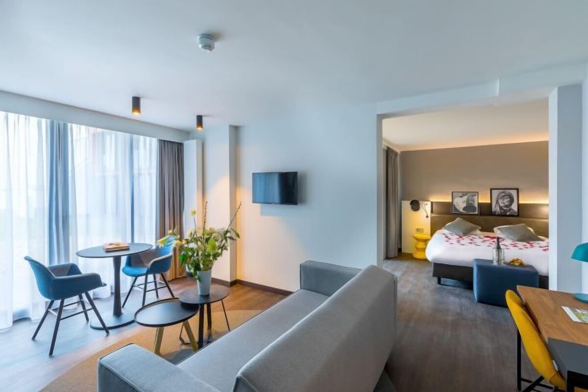 Ein modernes Hotelzimmer mit einer Couch, einem Esstisch und einem Bett mit Kopfteil.