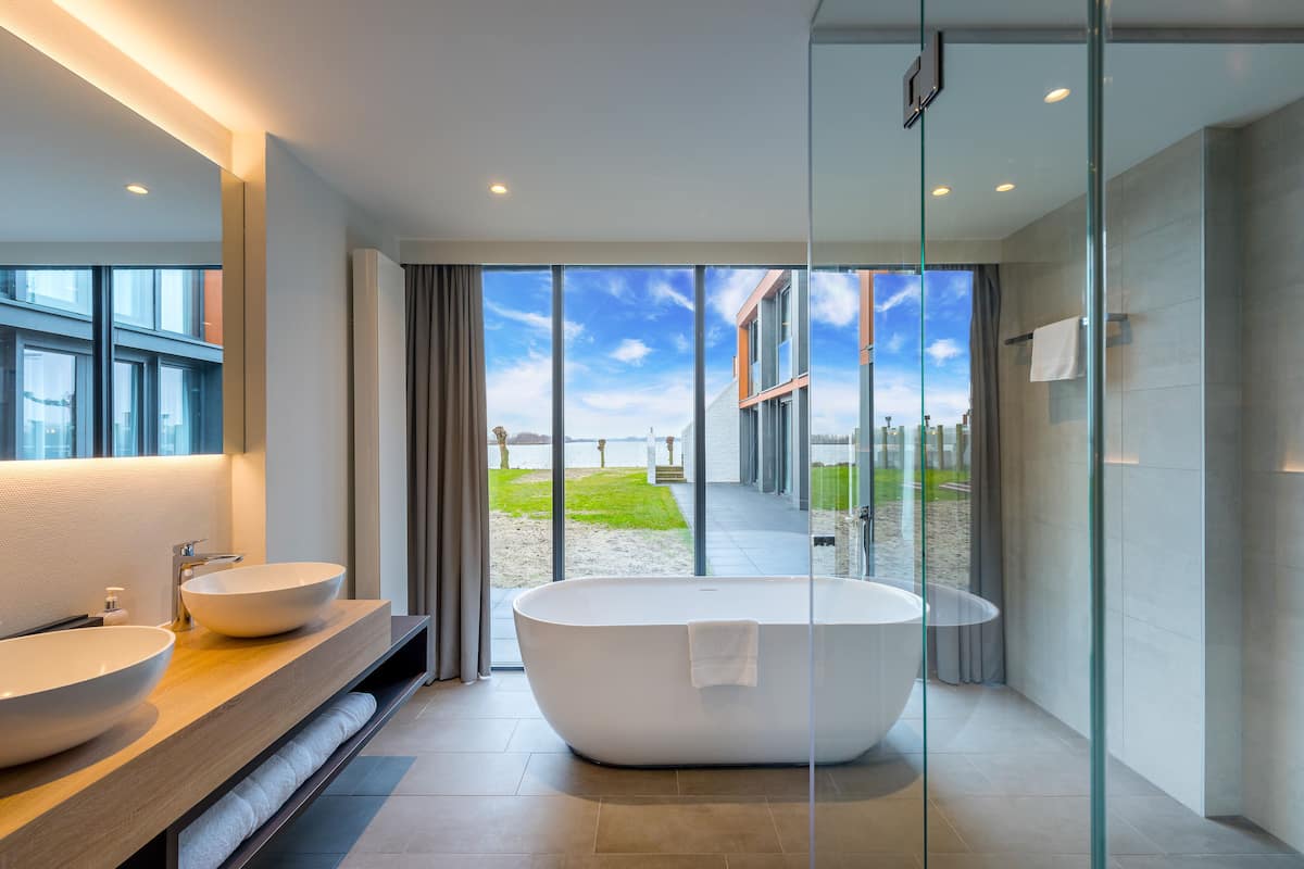 Une salle de bain moderne dotée d’une grande baignoire, de deux lavabos et d’une douche à parois de verre.