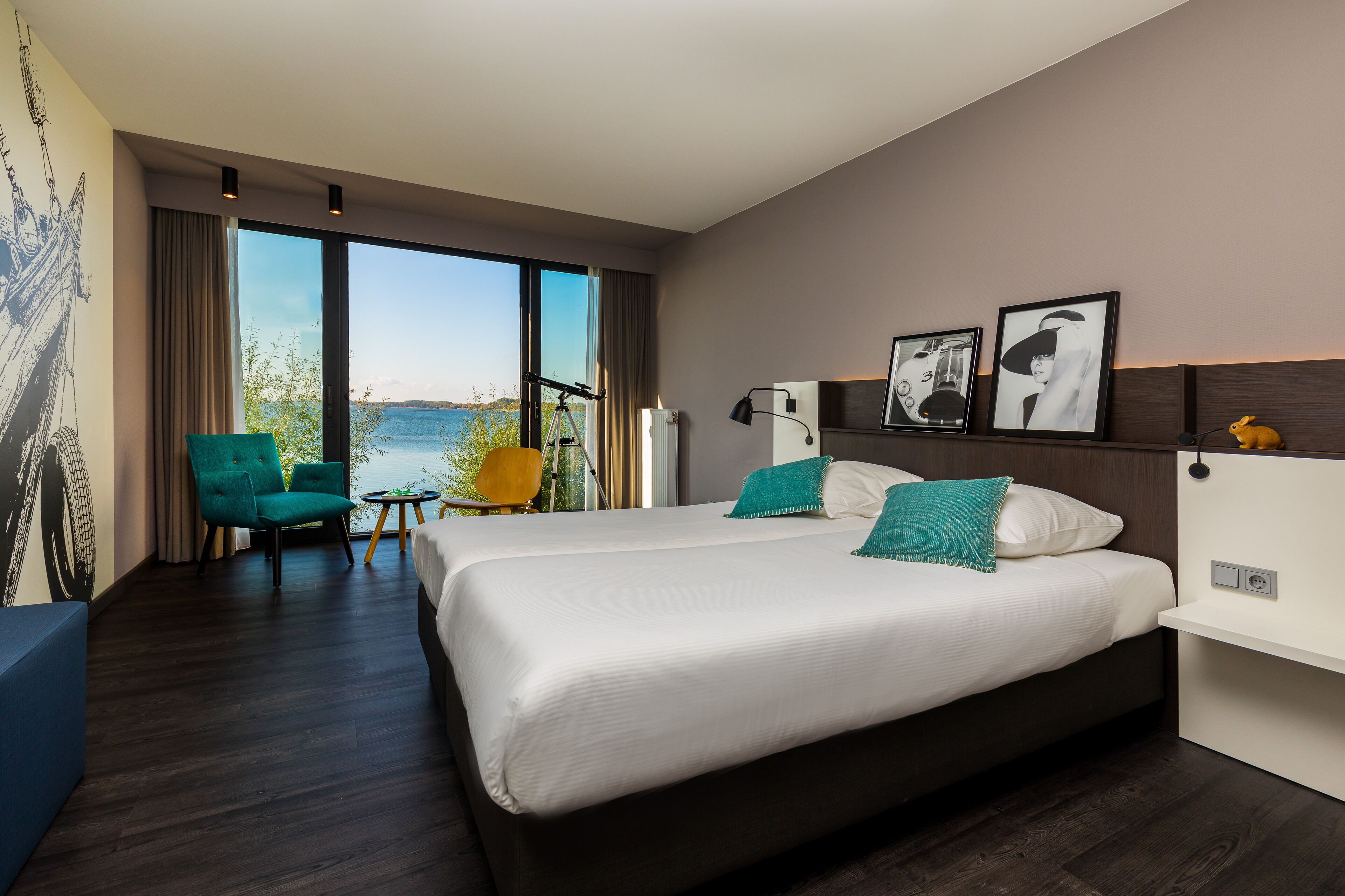 A modern hotel room with a large bed, a seating area with a chair, and a view of the sea.