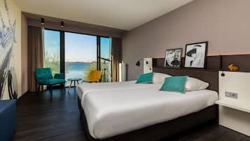 A modern hotel room with a large bed, a seating area with a chair, and a view of the sea.