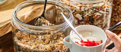 Una persona sosteniendo un tazón de yogur con granola y frutos rojos, con una cuchara adentro.