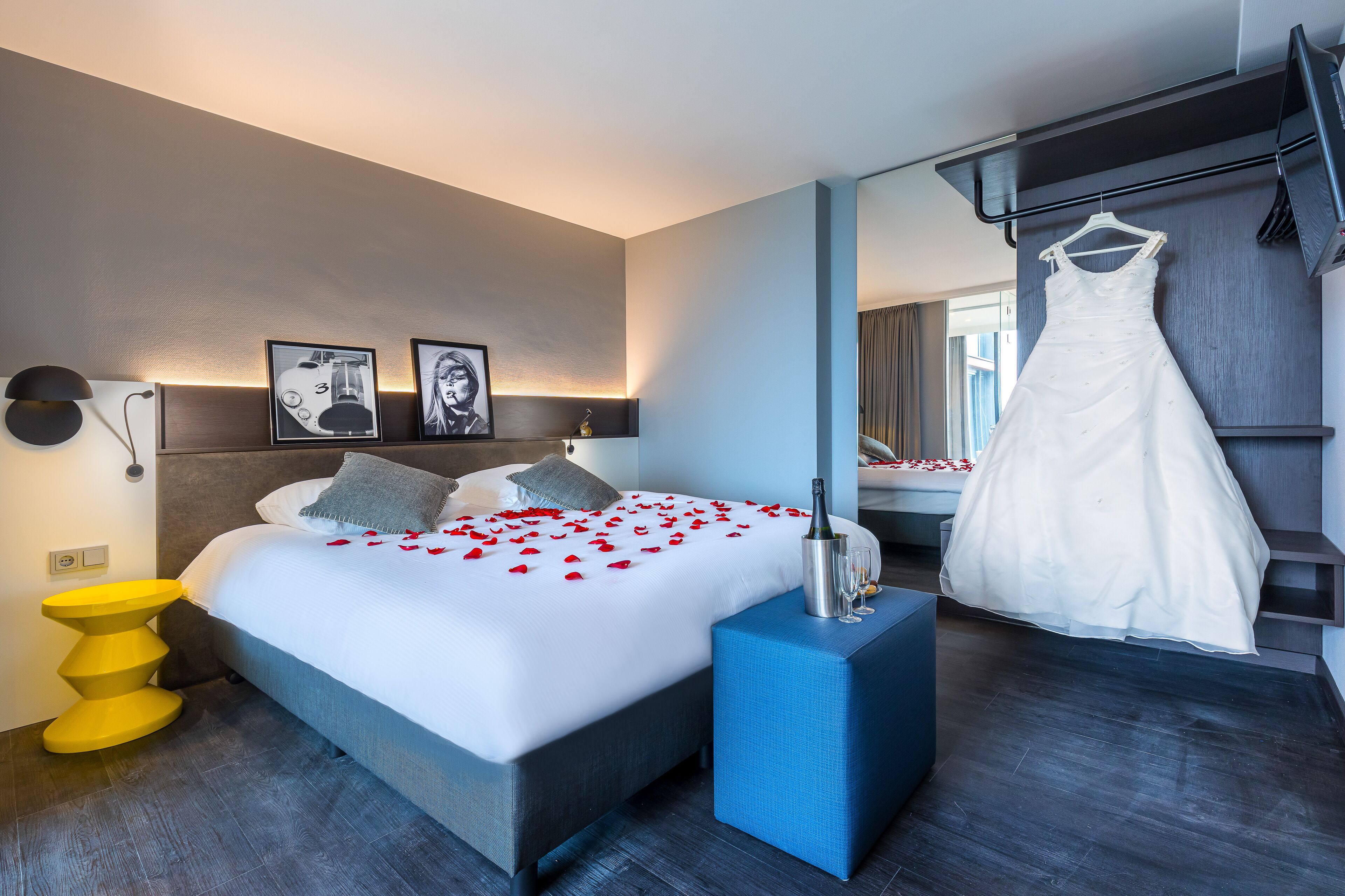 Een moderne hotelkamer met een groot bed, een nachtkastje, een spiegel en een hangende jurk.