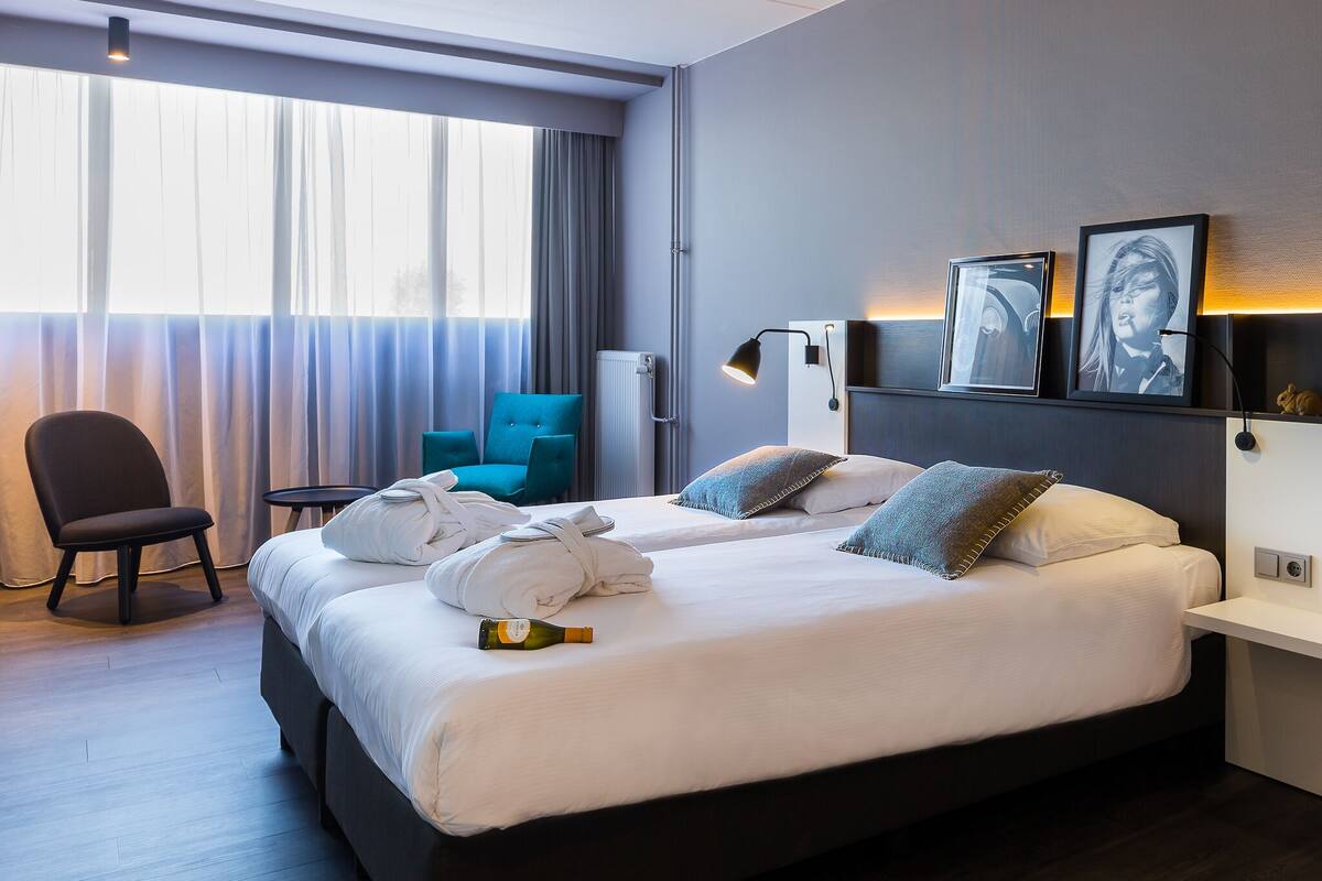 Une chambre d’hôtel avec un grand lit, une chaise, un bureau et une fenêtre avec des rideaux.