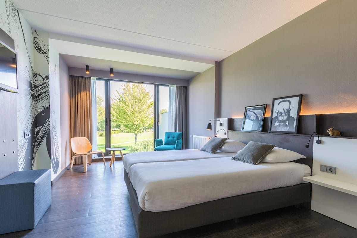 Une chambre d’hôtel moderne dotée d’un grand lit, d’un coin salon avec un fauteuil et d’une vue sur l’extérieur.