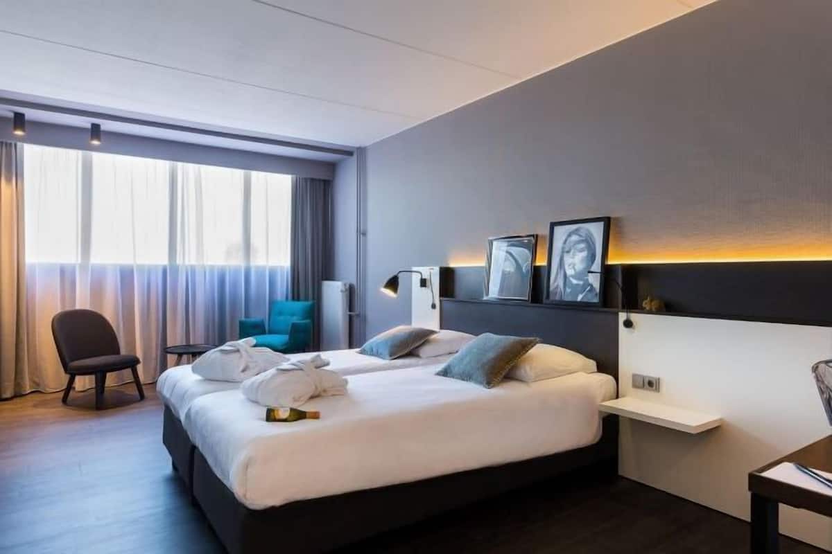 Une chambre d’hôtel avec un grand lit, une chaise, un bureau et une vue sur la ville par la fenêtre.