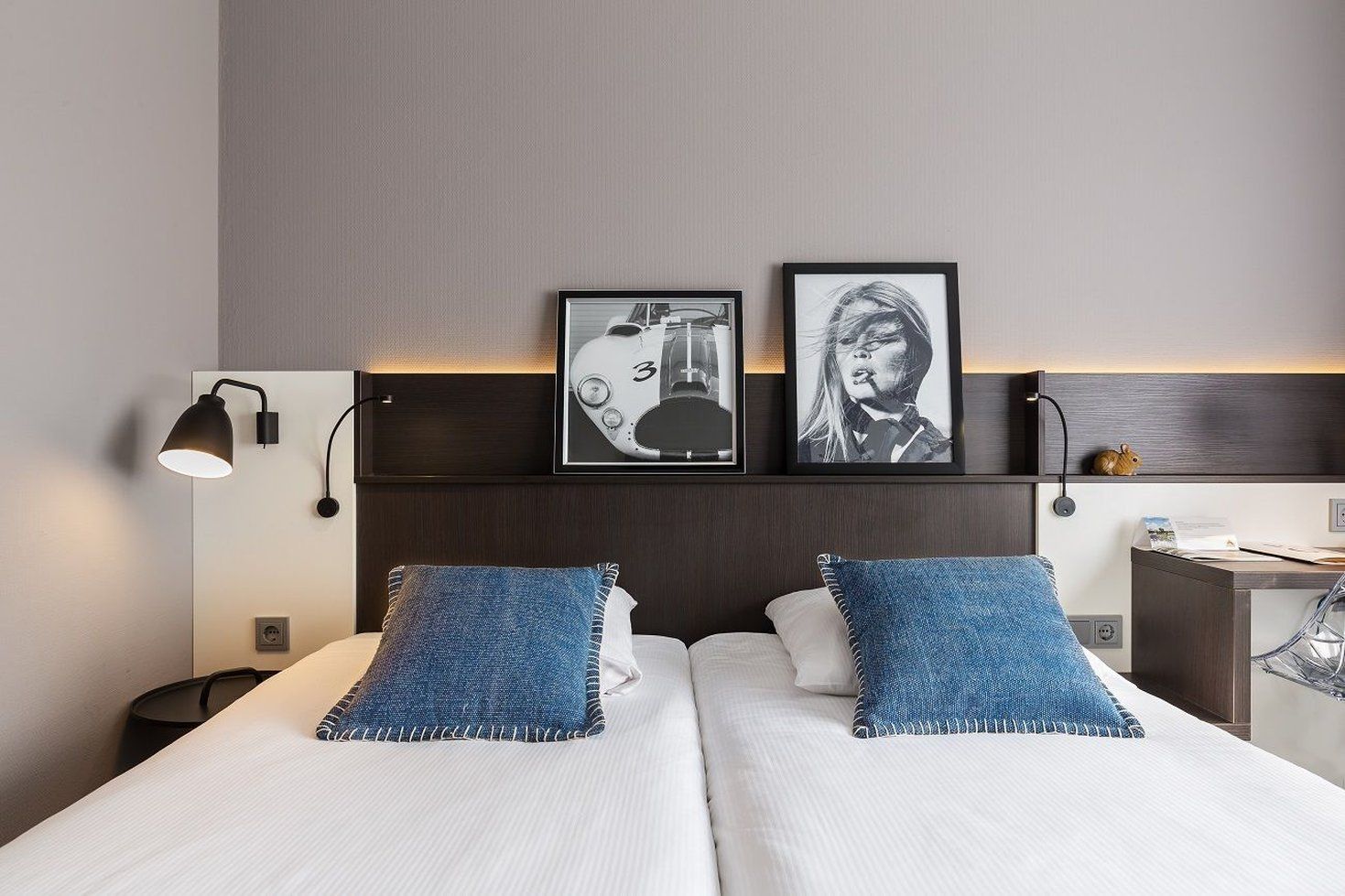 A hotel room with a bed, two pillows, a nightstand, a lamp, and two framed pictures on the wall.