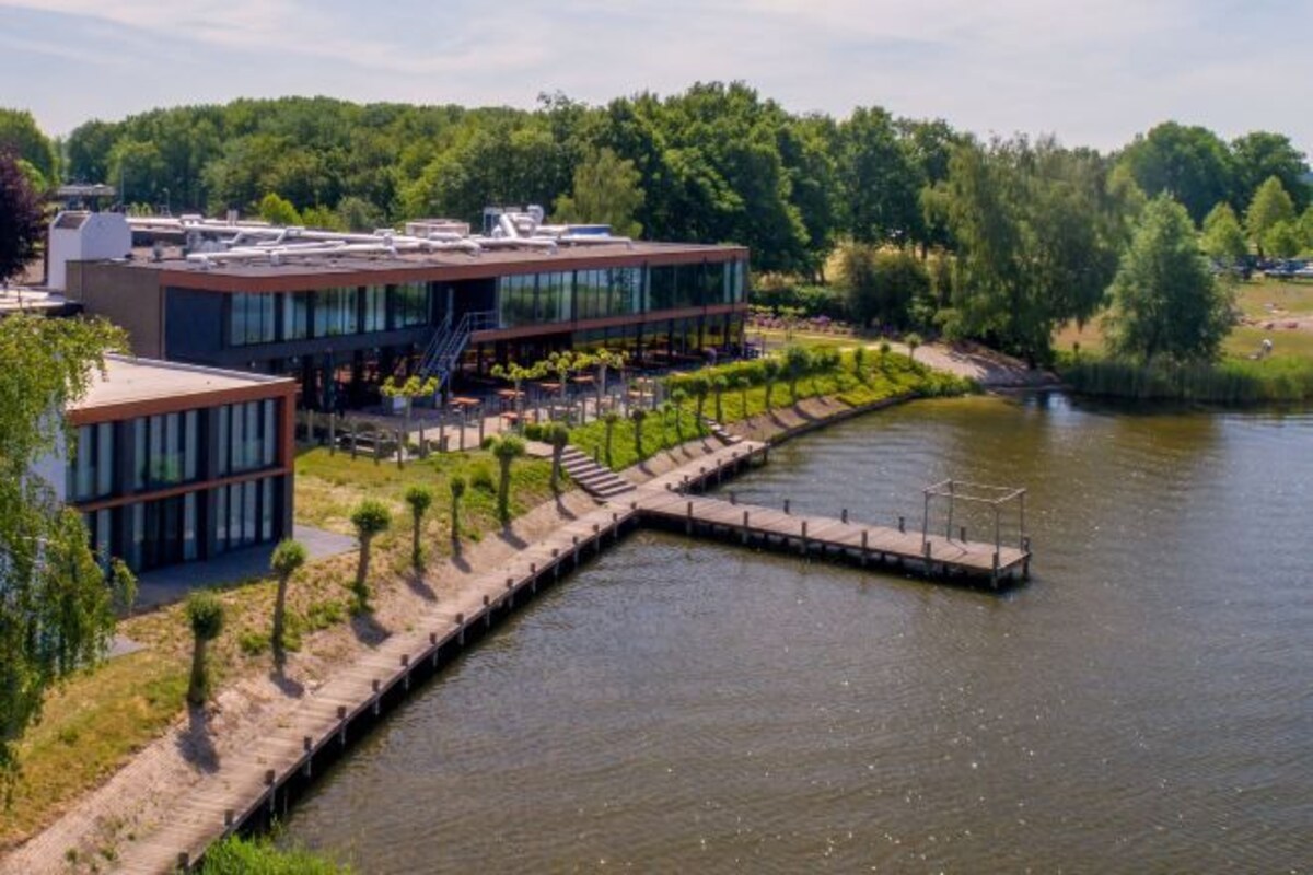 Un bâtiment moderne à la façade de verre, une jetée qui s’avance dans un lac et, au fond, une zone boisée.