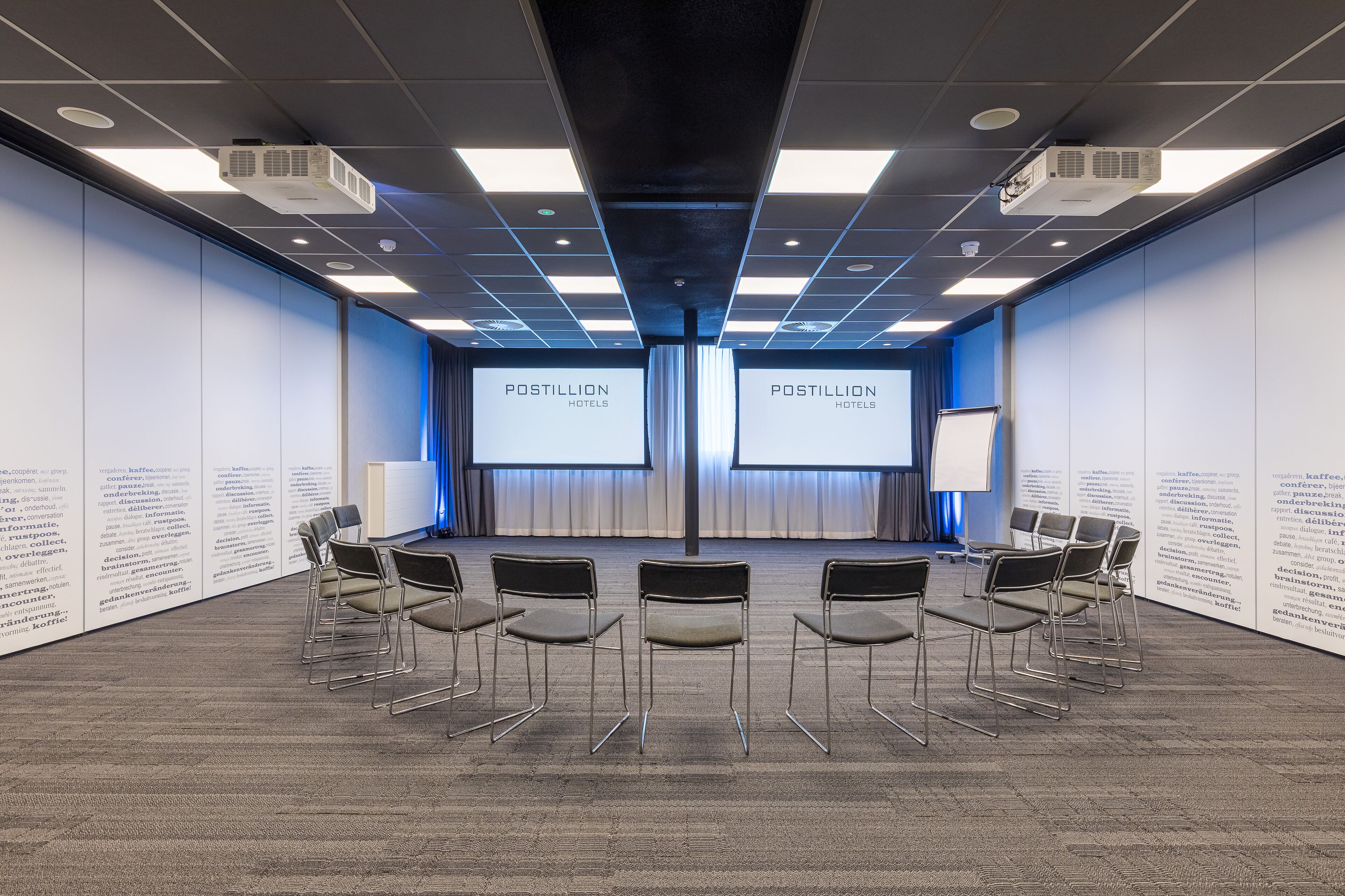 A conference room with a stage, chairs, and screens displaying 'POSTILLION HOTELS'.