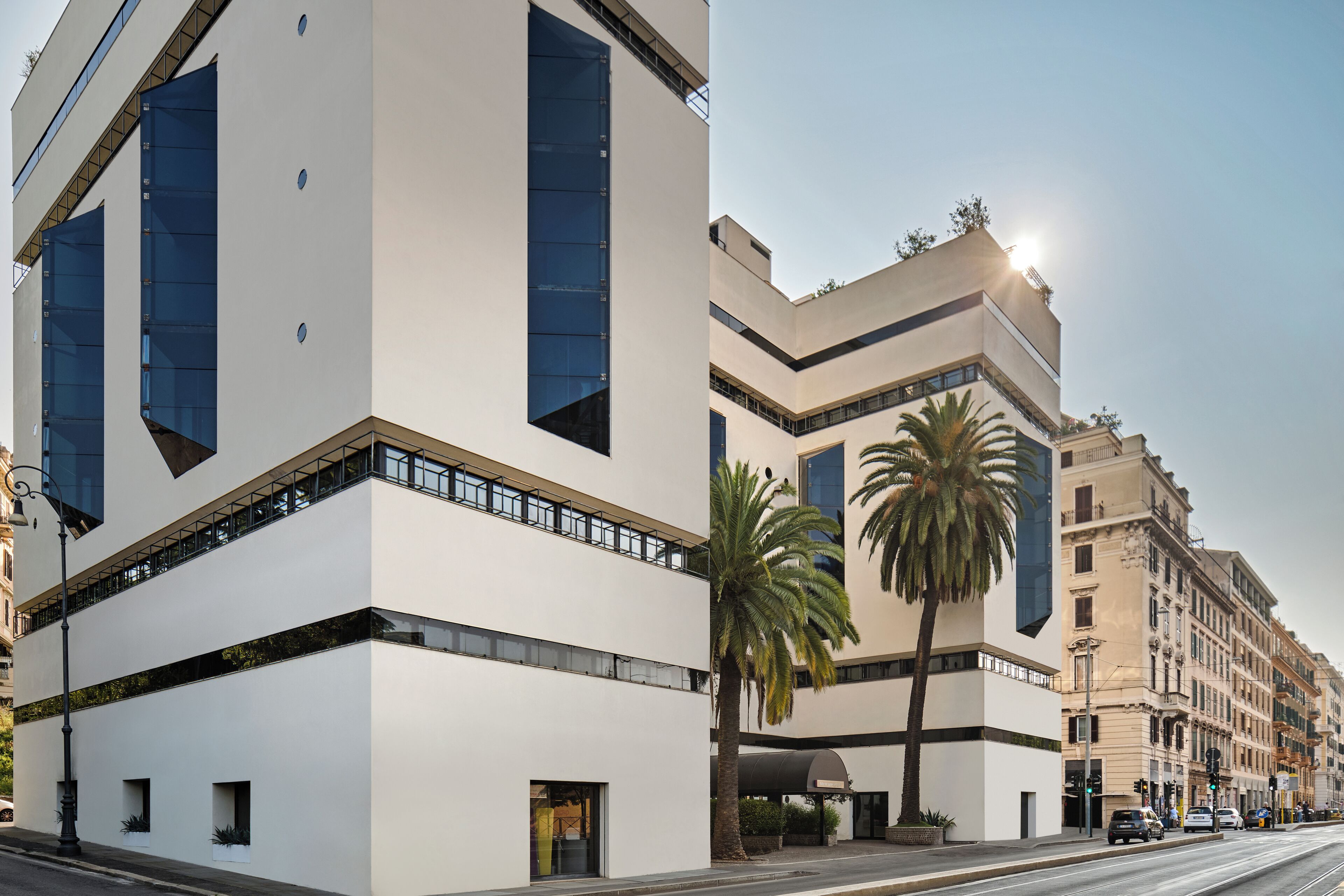 A modern building with large windows and a flat roof, located on a street with palm trees and other buildings.